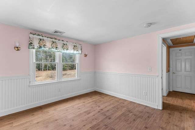 unfurnished room with wainscoting, wood finished floors, visible vents, and attic access