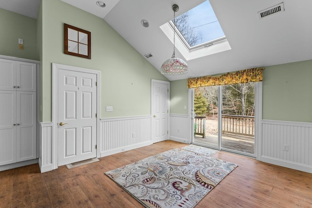 interior space featuring lofted ceiling with skylight, visible vents, wood finished floors, and wainscoting