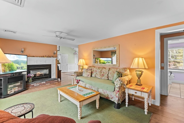 living area featuring a ceiling fan, a glass covered fireplace, visible vents, and wood finished floors