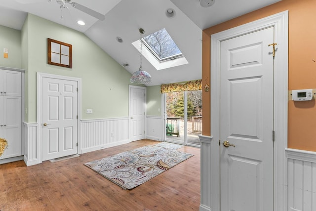 interior space featuring a ceiling fan, vaulted ceiling with skylight, a wainscoted wall, and wood finished floors