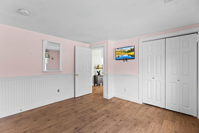 unfurnished bedroom featuring a wainscoted wall, a closet, and wood finished floors