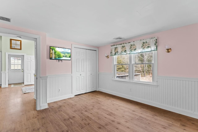 unfurnished bedroom with light wood finished floors, visible vents, and wainscoting