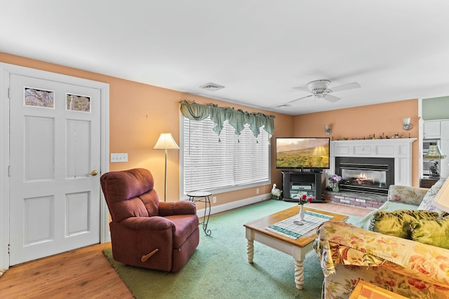 living room with ceiling fan, wood finished floors, visible vents, baseboards, and a glass covered fireplace