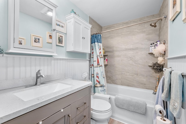 full bath featuring vanity, shower / tub combo, wainscoting, and toilet