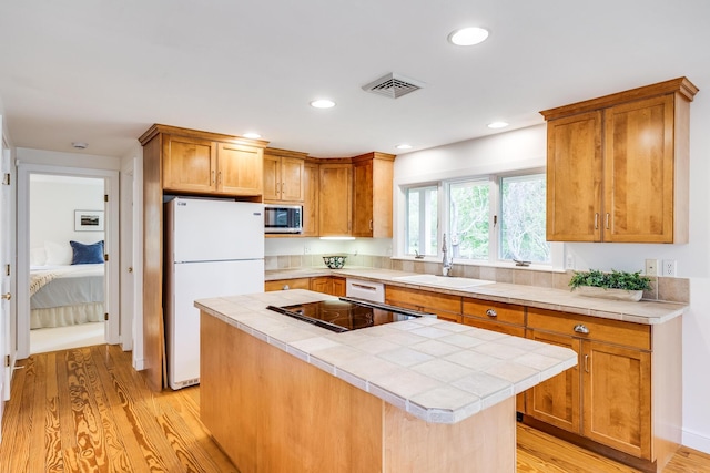 kitchen featuring white appliances, a sink, tile countertops, light wood-type flooring, and a kitchen island