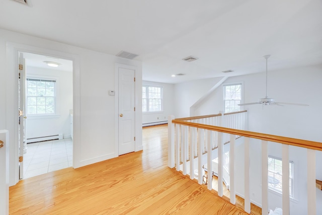 hall featuring a baseboard radiator, light wood-style flooring, an upstairs landing, and baseboards