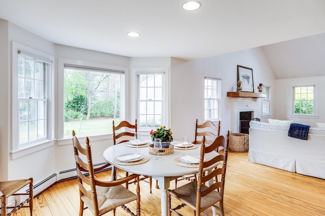 dining space featuring plenty of natural light, light wood-style floors, a fireplace, vaulted ceiling, and recessed lighting