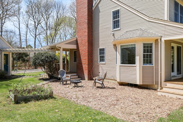 rear view of property with a chimney, a fire pit, a lawn, a pergola, and a garden
