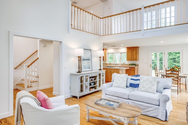 living area with a towering ceiling, stairway, light wood-style flooring, and baseboards