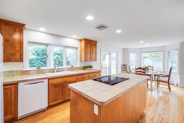 kitchen featuring dishwasher, a sink, tile counters, black electric stovetop, and light wood-style floors