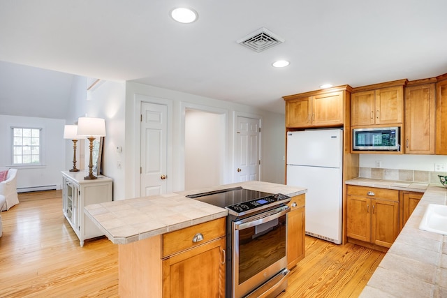kitchen featuring appliances with stainless steel finishes, tile countertops, light wood-type flooring, recessed lighting, and a center island
