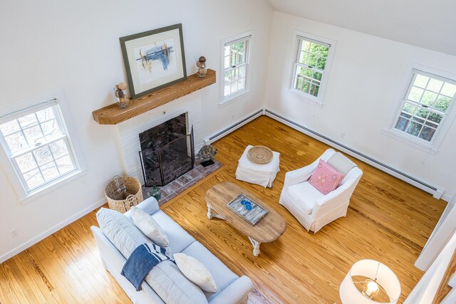 living room with a baseboard heating unit, wood finished floors, a fireplace, baseboard heating, and baseboards