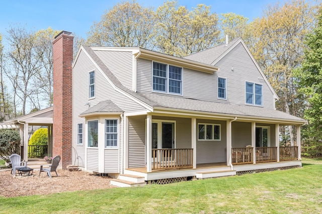 rear view of property featuring a fire pit, a chimney, a yard, a porch, and a shingled roof