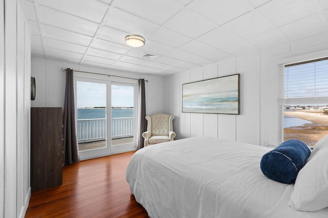bedroom featuring wood finished floors, a water view, access to exterior, visible vents, and a paneled ceiling