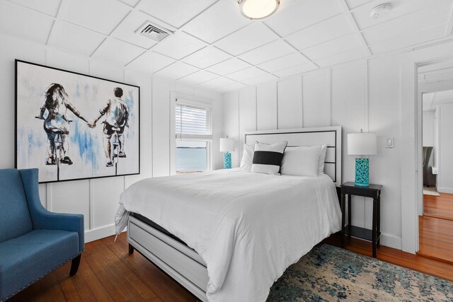bedroom with dark wood-style floors, a decorative wall, visible vents, and a paneled ceiling