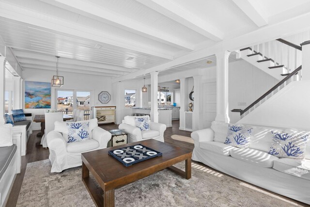 living area featuring beamed ceiling, wood finished floors, stairway, and ornate columns