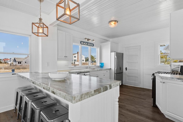 kitchen with white cabinetry, stainless steel appliances, a sink, dark wood-style floors, and a peninsula