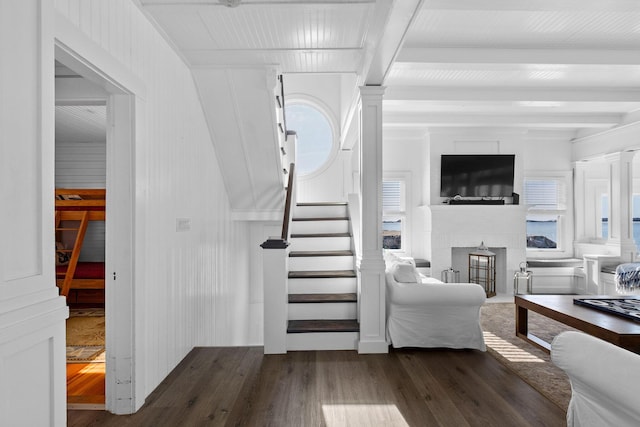 stairs featuring beam ceiling, a glass covered fireplace, and wood finished floors