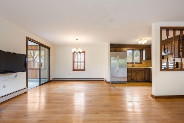 unfurnished living room with a baseboard radiator, a chandelier, light wood-style floors, and healthy amount of natural light