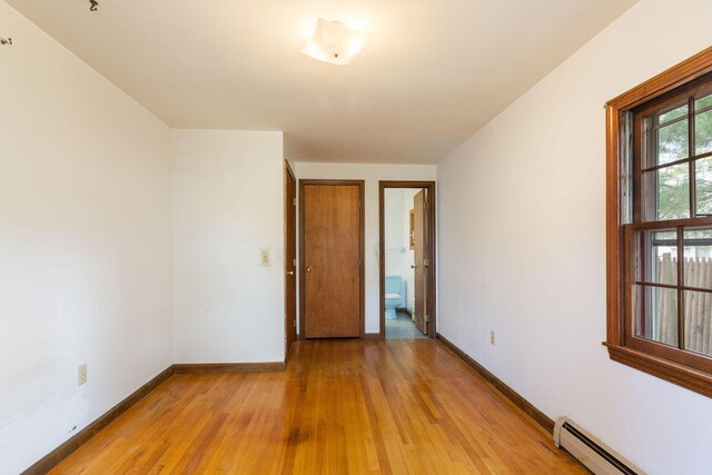 unfurnished room with baseboard heating, light wood-type flooring, and baseboards