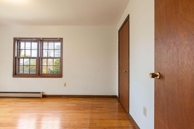 unfurnished room featuring a baseboard heating unit, light wood-style floors, and baseboards