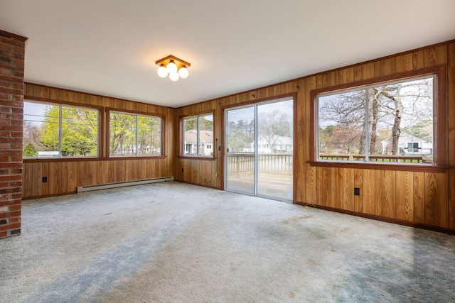 carpeted spare room with baseboard heating, wood walls, and baseboards