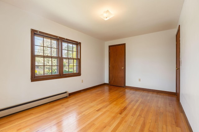 unfurnished room featuring a baseboard heating unit, light wood-style floors, and baseboards