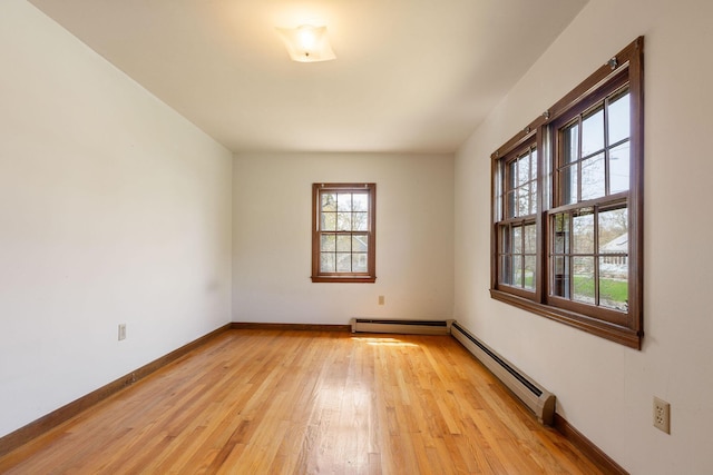 unfurnished room with a baseboard heating unit, light wood-style floors, and baseboards