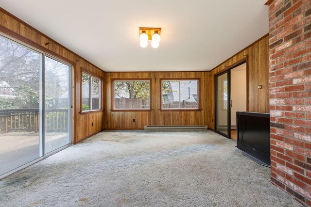 unfurnished sunroom featuring a baseboard heating unit, carpet flooring, and wooden walls