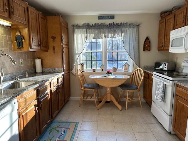 kitchen featuring backsplash, white appliances, light tile patterned flooring, and dark stone countertops