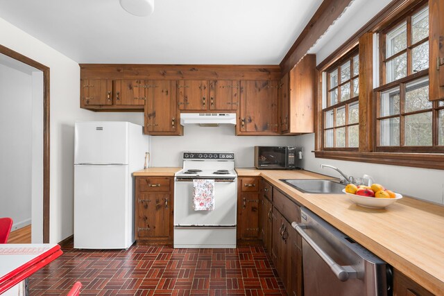 kitchen with white appliances, under cabinet range hood, a sink, brick patterned floors, and butcher block countertops