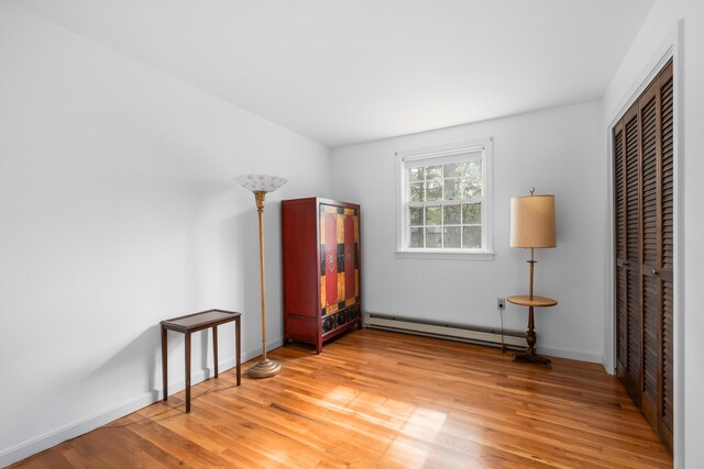 unfurnished room featuring a baseboard heating unit, light wood-style floors, and baseboards