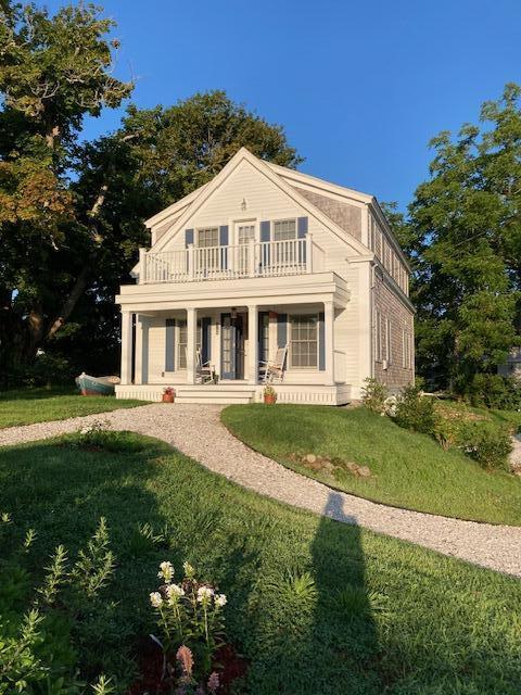 neoclassical home with covered porch, a front lawn, and a balcony