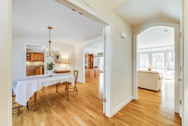 corridor featuring light wood finished floors, baseboards, arched walkways, and a notable chandelier