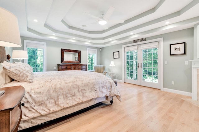 bedroom featuring light wood-style flooring, baseboards, access to exterior, french doors, and a tray ceiling