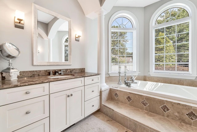 full bath featuring a tub to relax in, vanity, and decorative columns