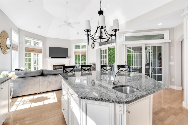 kitchen featuring light wood-style floors, a glass covered fireplace, open floor plan, a kitchen island with sink, and a sink