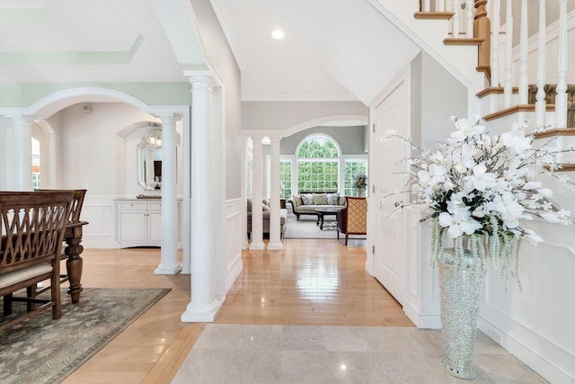 entryway with arched walkways, a wainscoted wall, light wood-type flooring, ornate columns, and a decorative wall