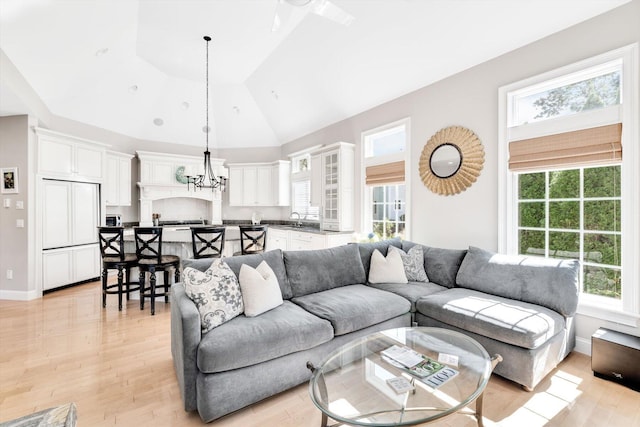 living room with light wood-style floors, high vaulted ceiling, baseboards, and an inviting chandelier