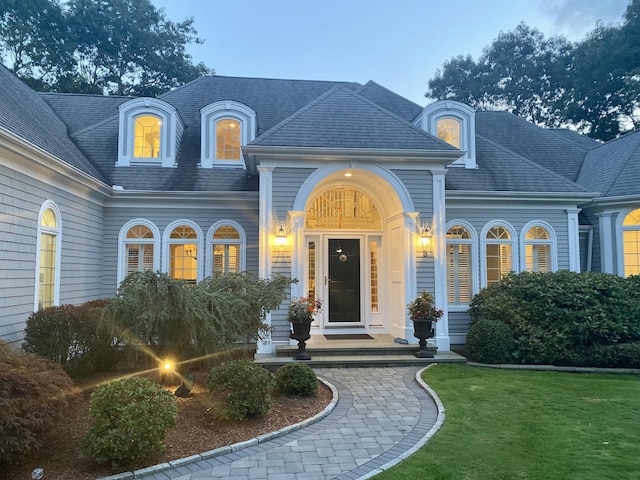 doorway to property with a shingled roof and a lawn