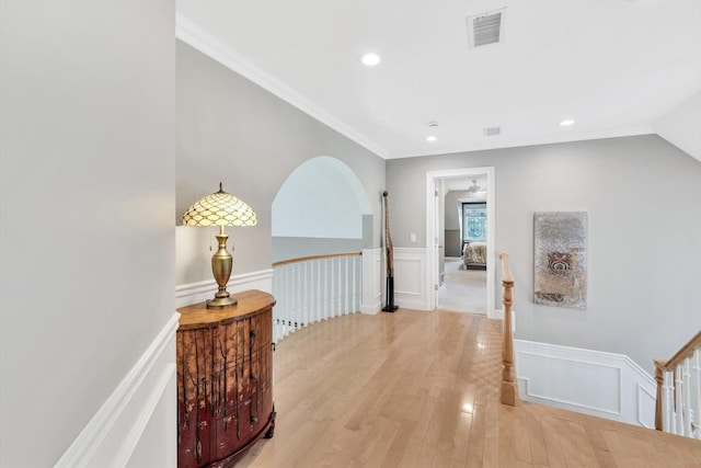 corridor with light wood-style floors, visible vents, crown molding, and wainscoting