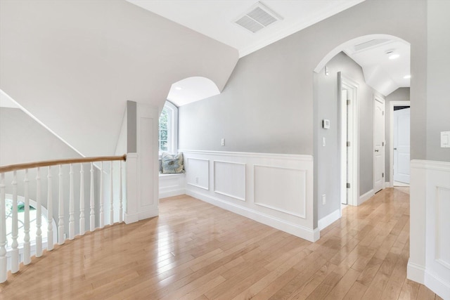 interior space featuring vaulted ceiling, a decorative wall, visible vents, and light wood-style floors