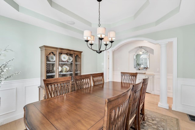 dining area with a chandelier, wainscoting, a raised ceiling, and decorative columns