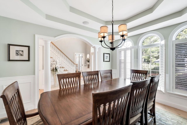 dining room featuring arched walkways, a notable chandelier, wainscoting, a tray ceiling, and decorative columns