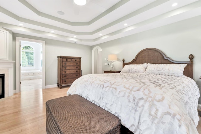 bedroom with arched walkways, recessed lighting, a fireplace, light wood-style floors, and a raised ceiling