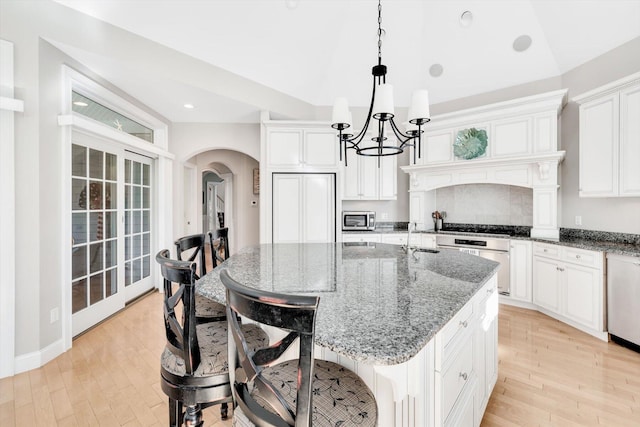 kitchen with wall oven, arched walkways, stainless steel microwave, light wood-type flooring, and stone counters