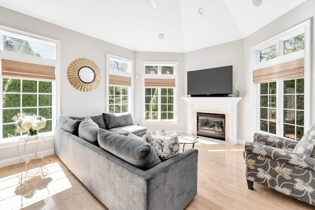 living area featuring high vaulted ceiling, light wood-type flooring, a fireplace with flush hearth, and baseboards