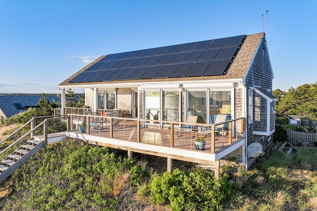 back of house with roof mounted solar panels, roof with shingles, and a wooden deck