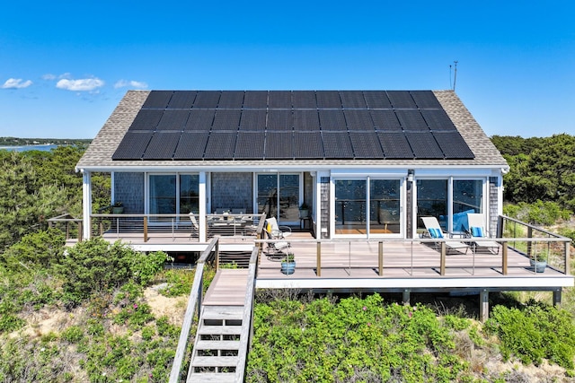 back of property with roof mounted solar panels, a deck, stairway, and a shingled roof