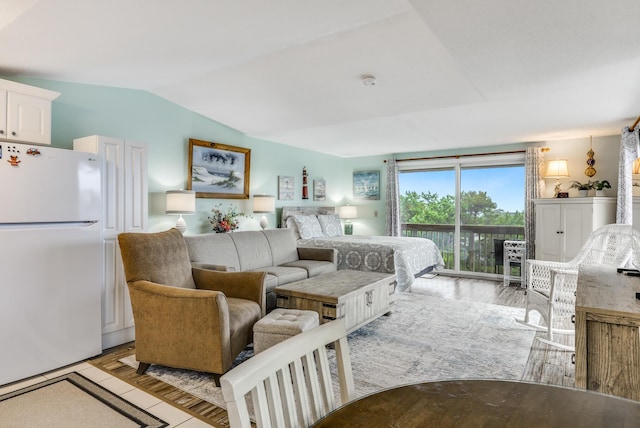 bedroom featuring access to exterior, light hardwood / wood-style flooring, vaulted ceiling, and white fridge